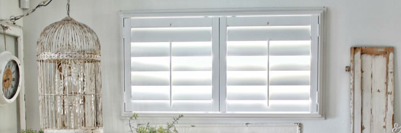 White outside-mounted Polywood shutters on a living room window with cottage decor